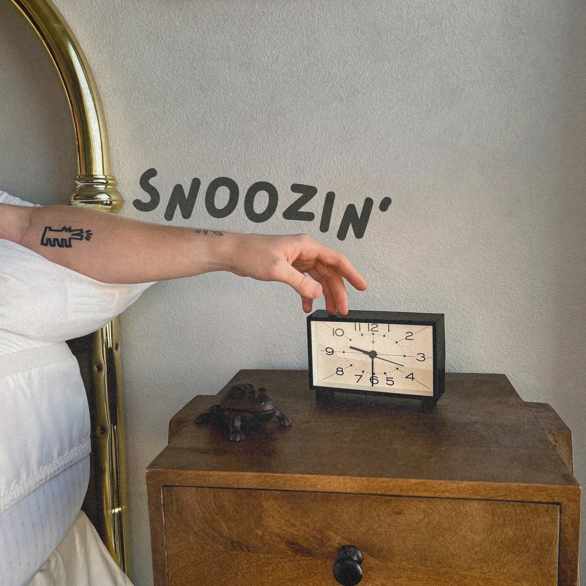 Cover of Snoozin': an arm reaching out of bed to an alarm clock on a wooden nightstand