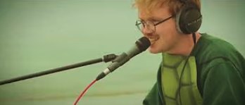 Geepers! singing into a mic in headphones and a turtle-shell shirt